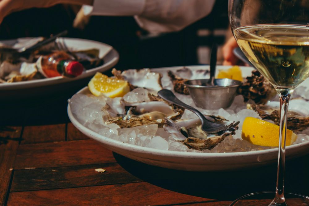 close up of a plate of oysters on a table with white wine